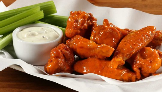Pile of buffalo wings next to a cup of ranch dressing and celery sticks