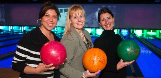 Gillian and two teammates holding bowling balls and smiling